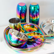 Set of colorful stainless steel dinnerware including plates, bowls, cups, forks, and spoons on a white background.