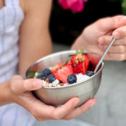 Child eating yogurt, granola, strawberries, and blueberries in 12 ounce stainless steel bowl with spoon