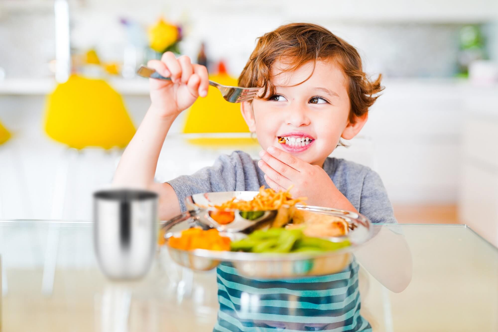 toddler boy eating meal on stainless steel plates with fork and cup