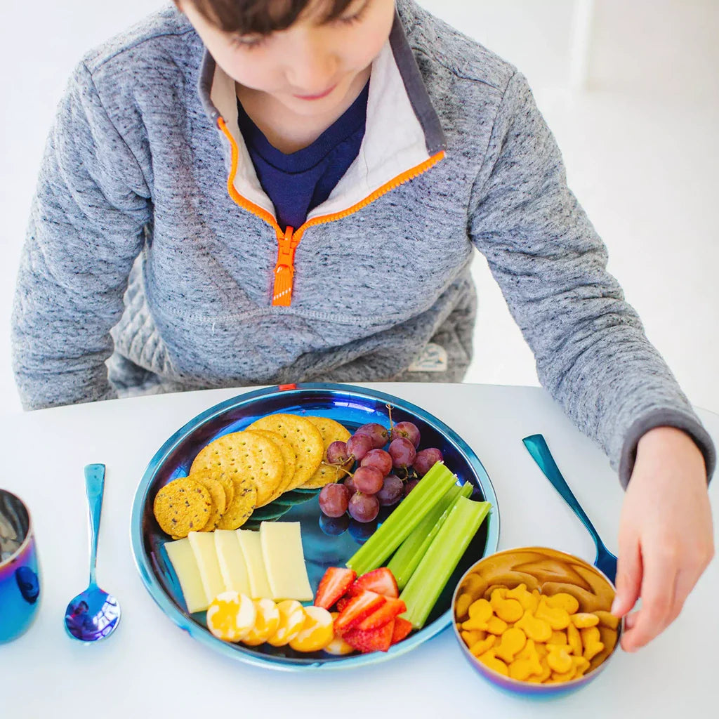 Kids stainless steel plates. Young child at table with a blue 9 inch Purposeful Plate, fork, spoon,  ounce Conscious Cup, and 8 ounce round bowl with crackers.