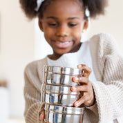 Child holding a stack of silver food containers.