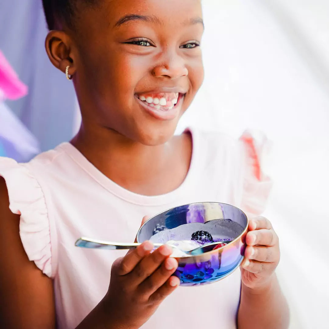 Little girl with a big smile eating yogurt and blackberries from an 8 ounce Iridescent-Blue round bowl and spoon.