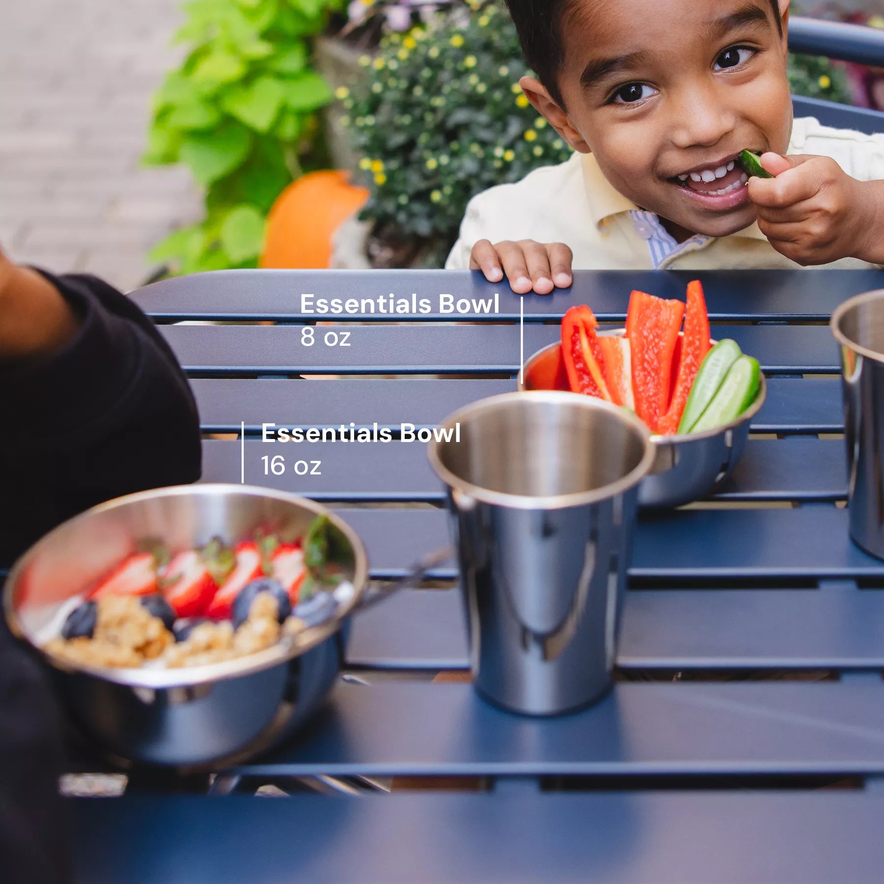 Happy kids eating snacks at a picnic table with Ahimsa's 8 ounce Essentials Bowl, 16 ounce Essentials Bowl, and 10 oz cup.  All dishes are dishwasher safe, stainless steel, durable, and loved by families.