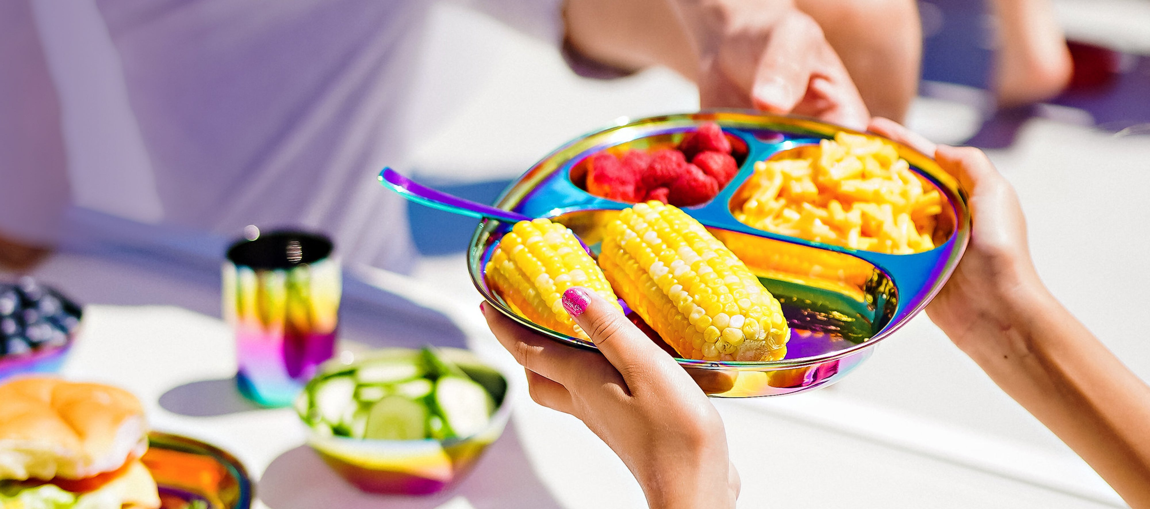 Balanced Bites stainles steel divided compartment plate with corn, raspberries, and pasta at a backyard barbeque. The perfect plates for poolside, outdoors, or indoors.