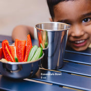 Happy child with a stainless steel bowl of vegetables and a stainless steel 10 ounce cup on a table, with 'Essentials Bowl 8 oz' text.
