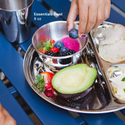 8 ounce stainless steel bowl nested in a round divided compartment plate next to a 10 ounce cup. The bowl and plate have a rainbow of fruits, including blueberries, avocado, strawberries, and blackberries. All Ahimsa dishes are dishwasher safe, Made Safe certified, and loved by families. 