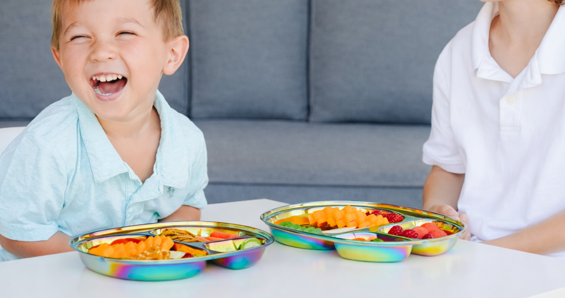 Two children sitting at a table with colorful plates of fruit and cheese on Rainbow stainless steel Balanced Bites plates.