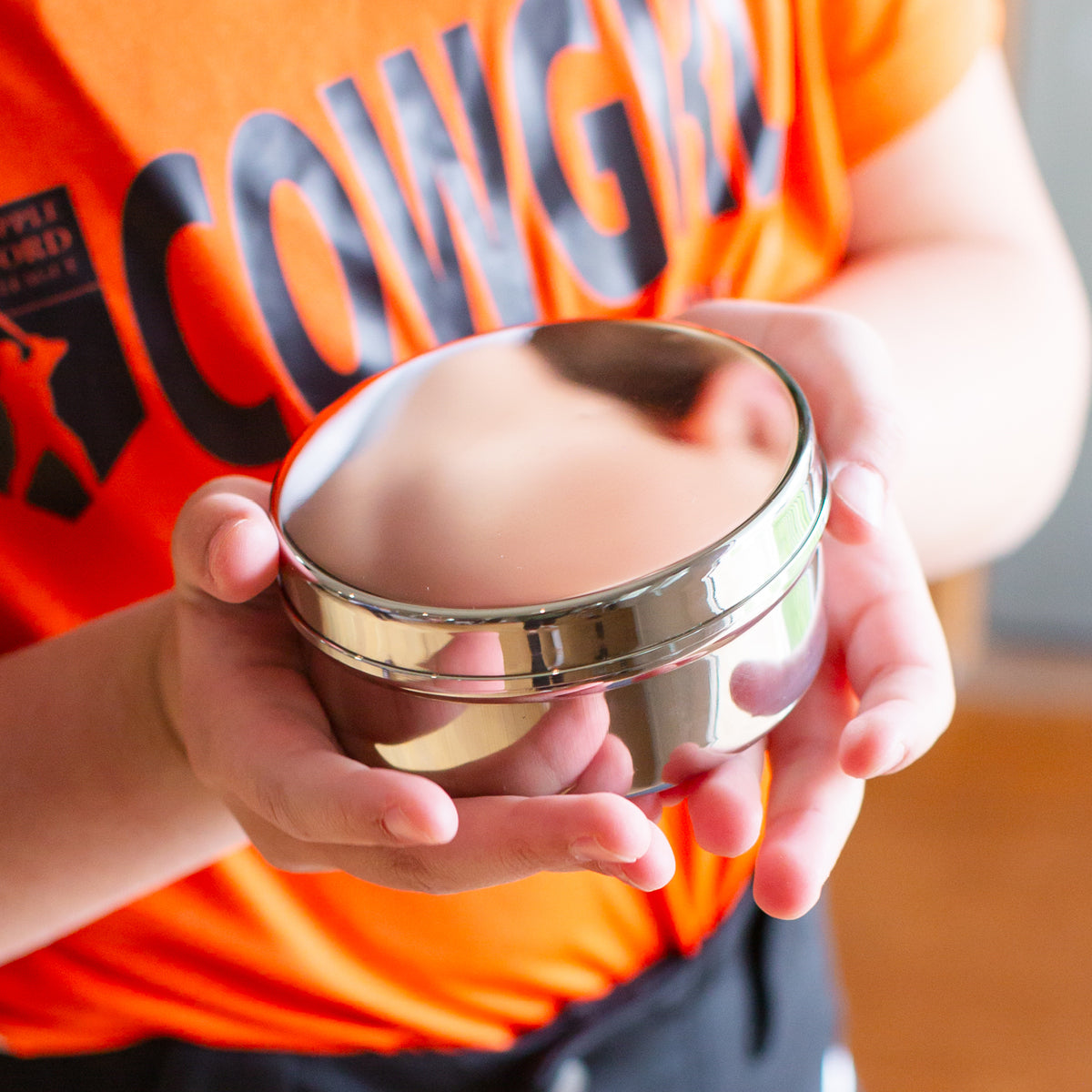 Child holding stainless steel circle container for lunches, snacks, and on-the-go