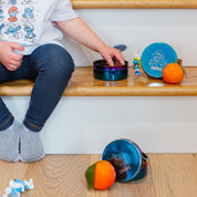 Child playing with colorful Smurf-themed toys, wearing a Smurfs shirt, and blue stainless steel food containers with fruit