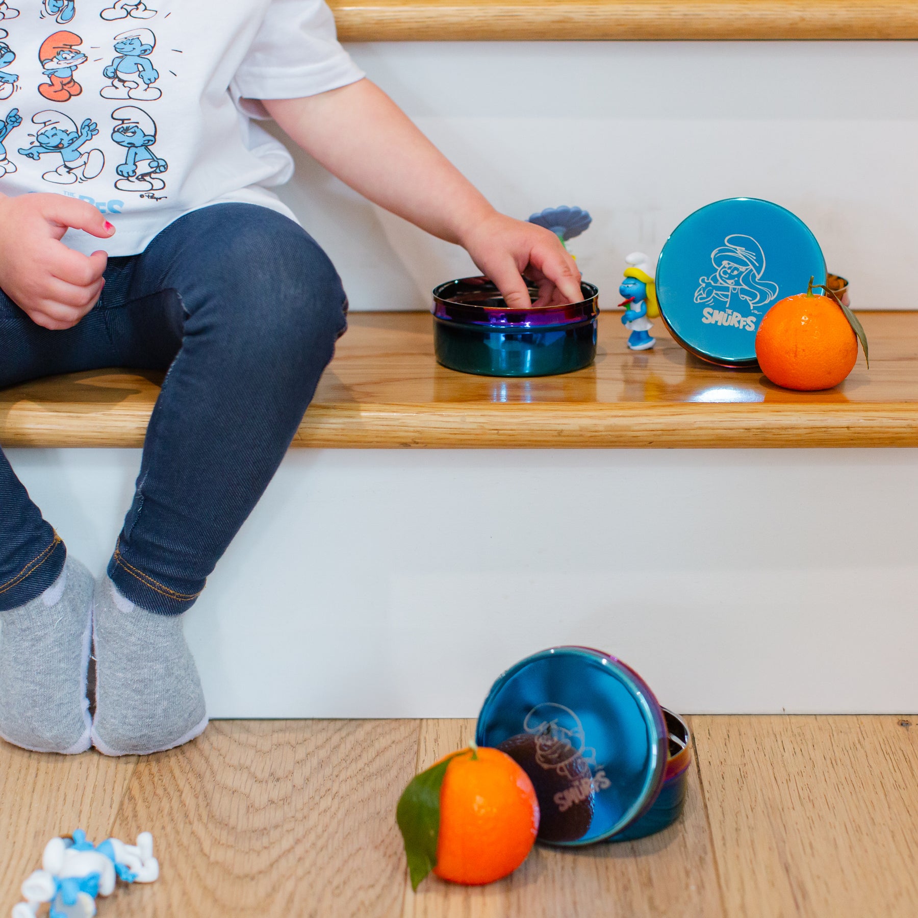 Child playing with colorful Smurf-themed toys, wearing a Smurfs shirt, and blue stainless steel food containers with fruit