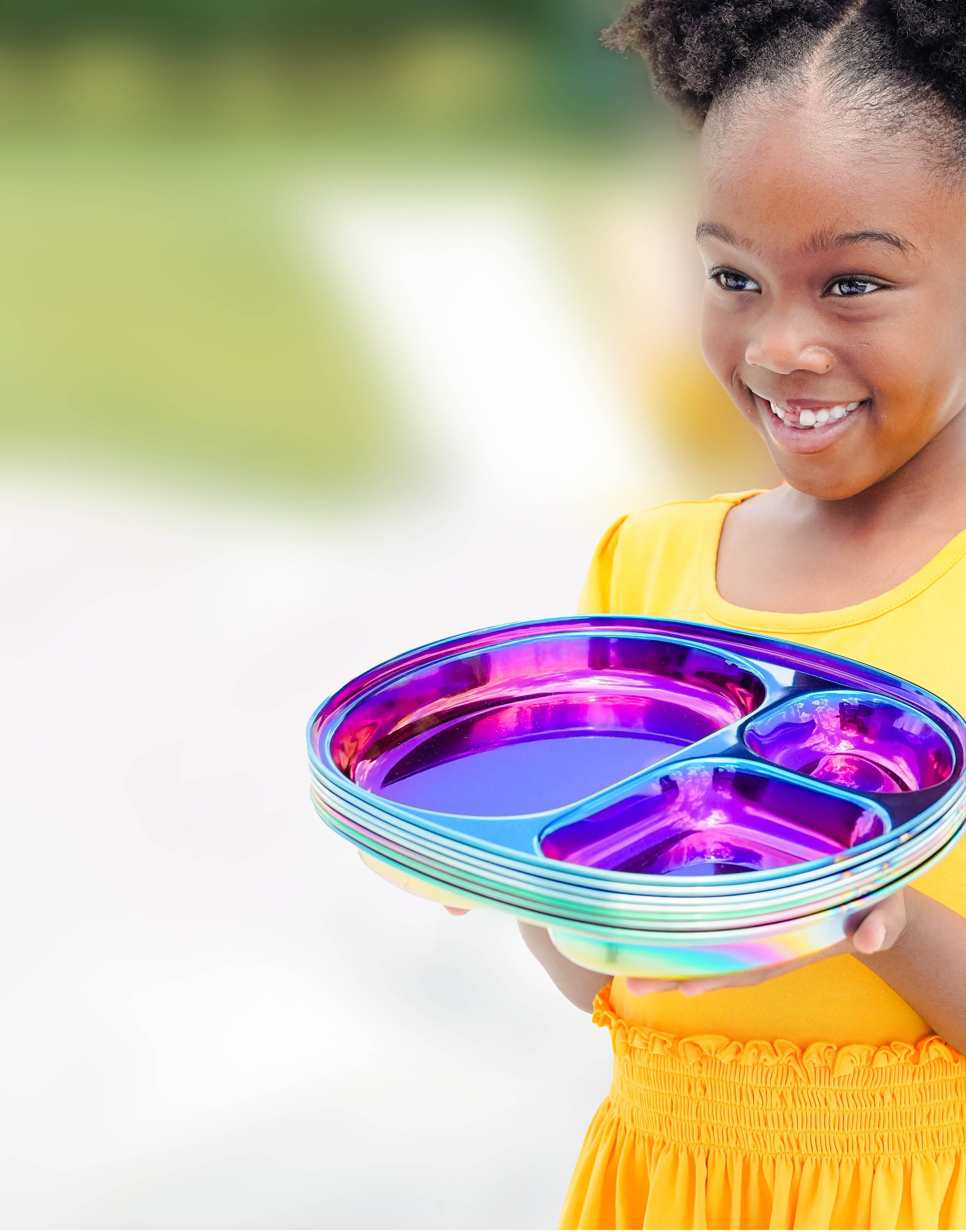 Little girl holding a stack of stainless steel compartment plates, Ahimsa's Balanced Bites compartment plates in Iridescent Blue