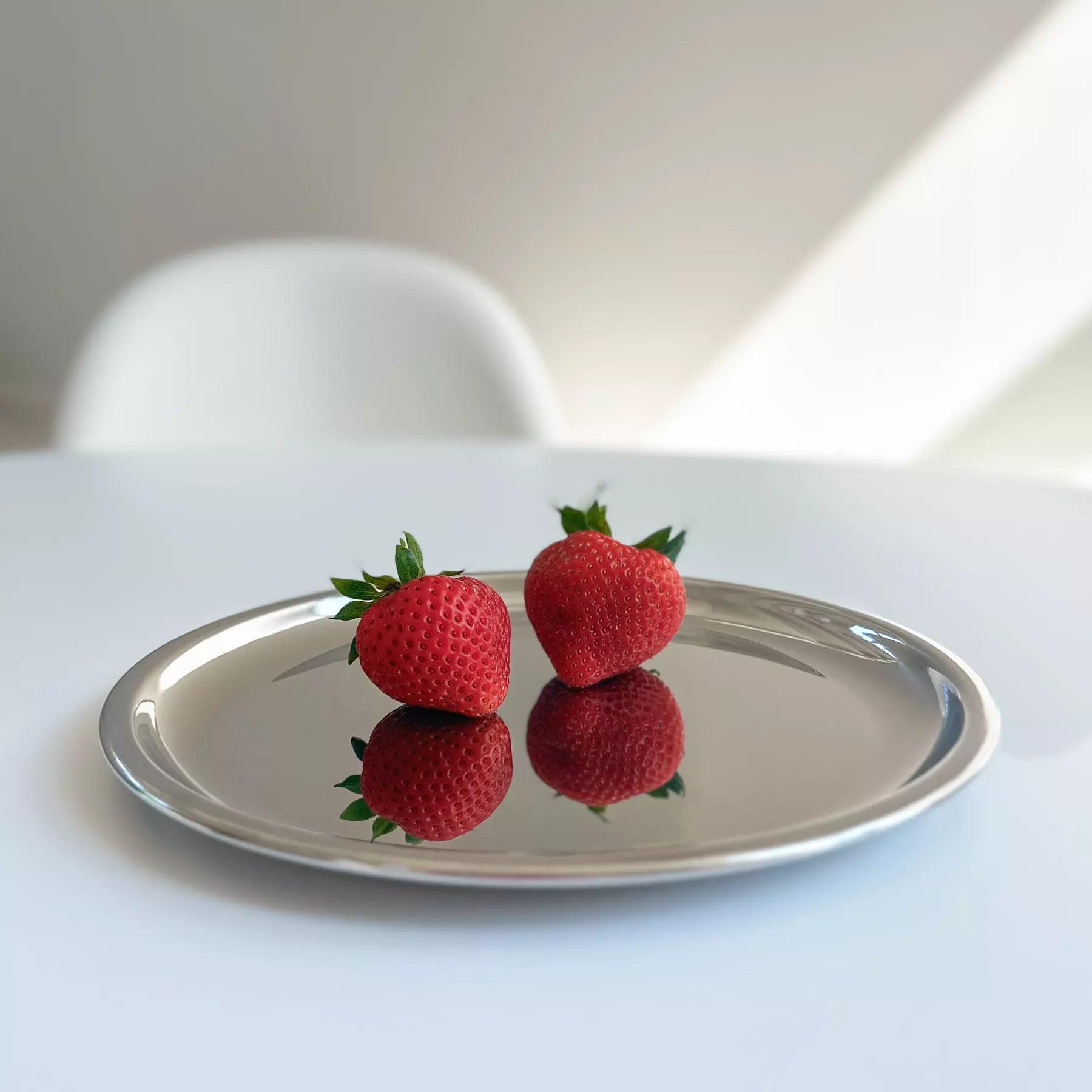 9 inch round stainless steel plate on a table with 2 strawberries on it, showing their reflection