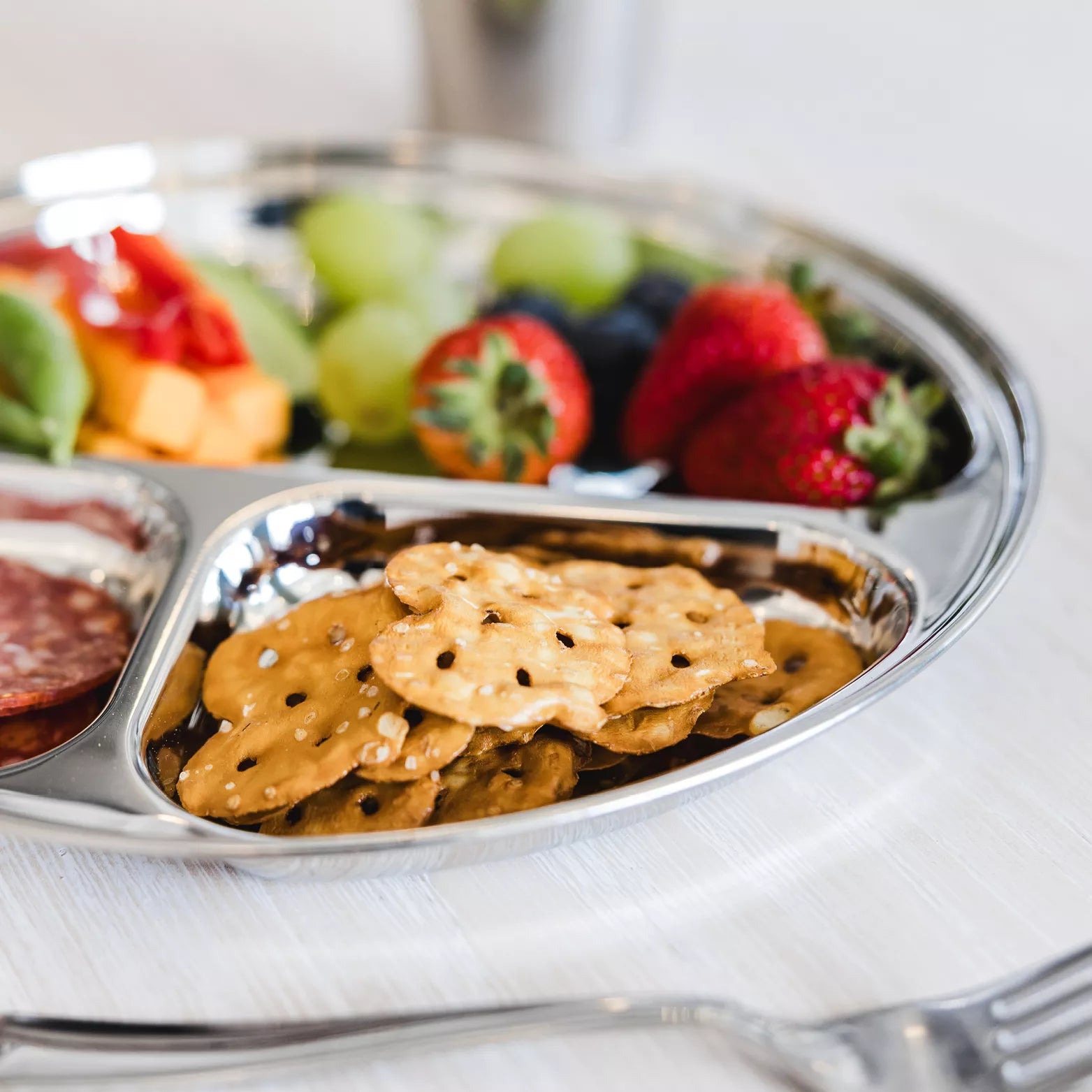 Stainless steel plate for toddlers and kids. Round compartment plate with fruits and snacks.