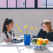 Dishes kids love that also match your kitchen! Two children sitting at a table with a vase of flowers and a fruit bowl. The kids have stainless steel dishes including graphite Purposeful Plates, forks, and spoons.