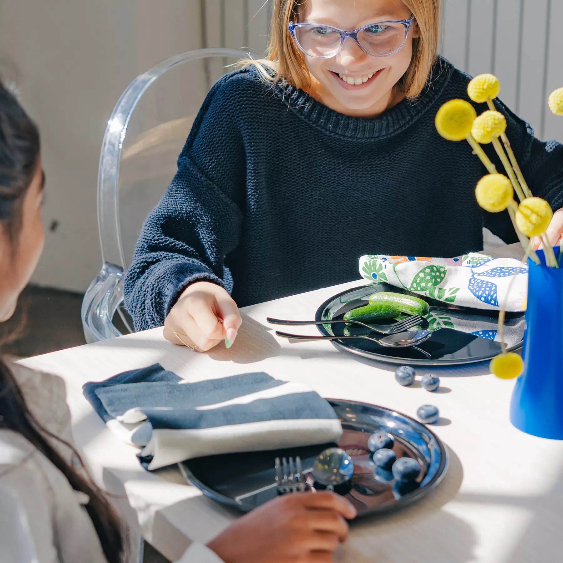 Twokids sitting at a table with plates, cutlery, and decorative items. The dishes are Ahimsa's stainless steel dishes in graphite - perfect for toddlers, kids, and adults. 