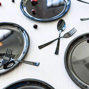 Graphite Ahimsa Purposeful plates and silverware on a white tablecloth. Ahimsa's dishes are made of stainless steel - the American Academy of Pediatrics recommends stainless steel because it does not transfer harmful chemicals into our children's food - plus these dishes are gorgeous and they match your kitchen!