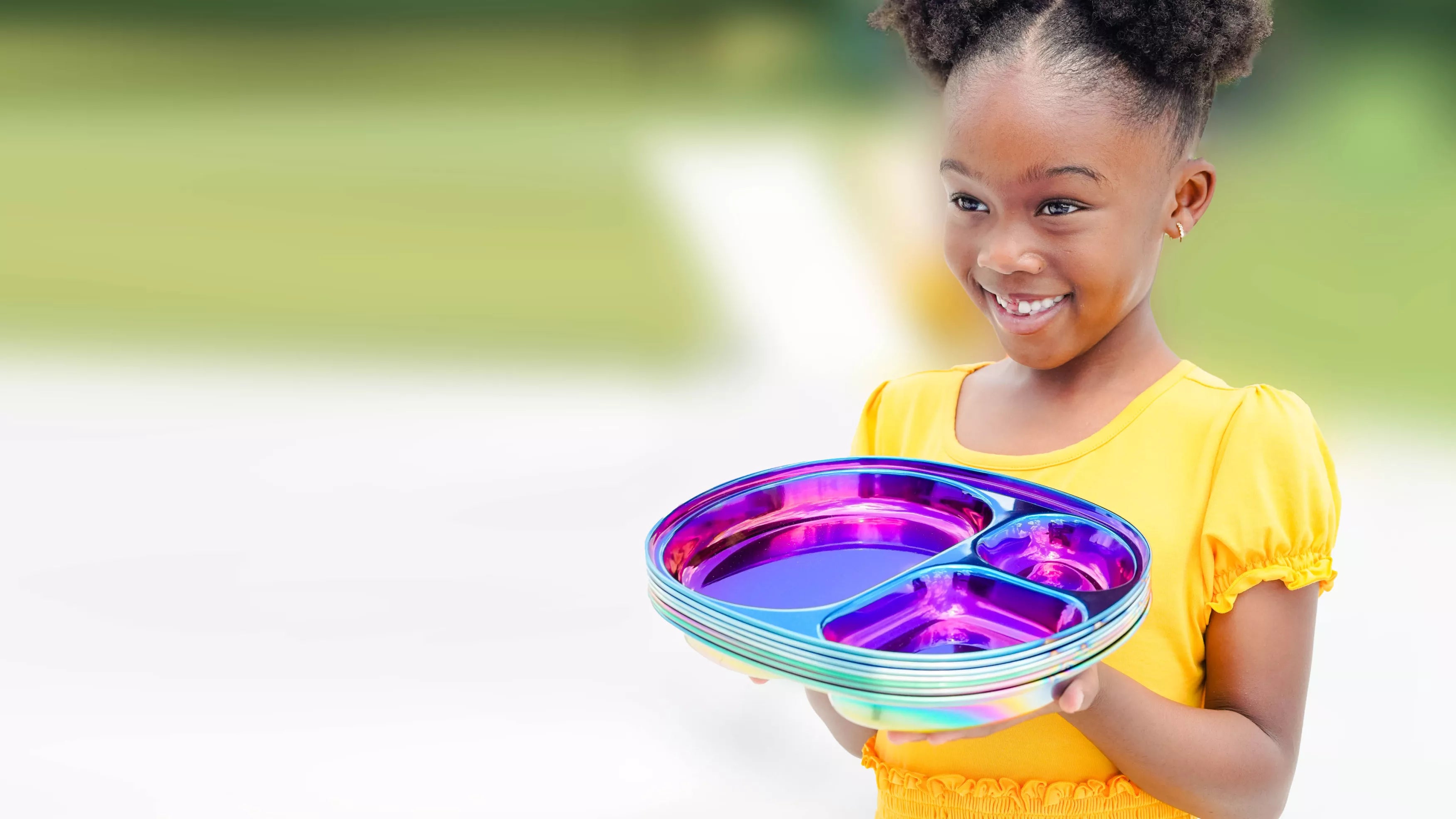 Girl in yellow dress holding colorful stainless steel divided plates for kids